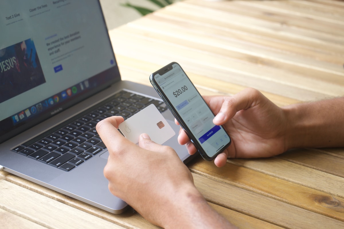Pessoa usando smartphone e cartão de crédito ao lado de um laptop, representando serviços financeiros digitais e portabilidade de crédito