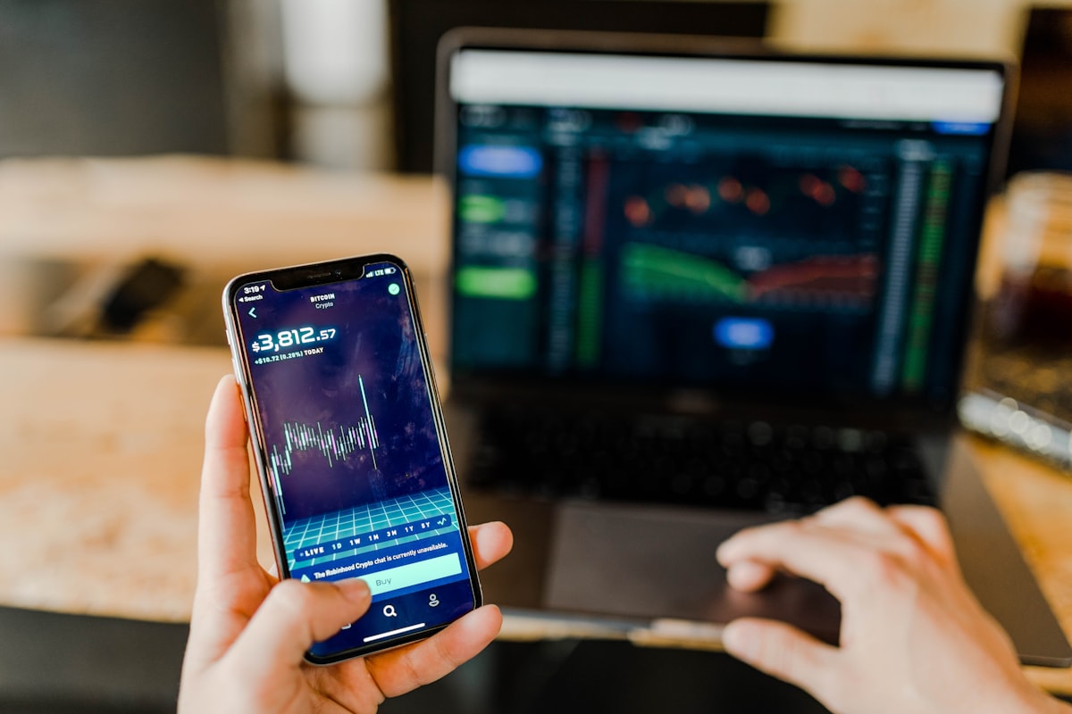 Pessoa utilizando smartphone e laptop simultaneamente para operações financeiras digitais