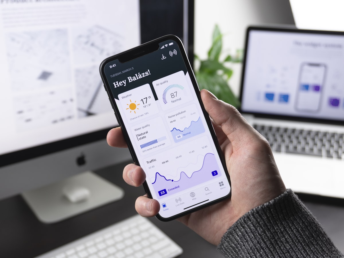 Pessoa segurando smartphone com painel de dados e gráficos em tempo real na tela