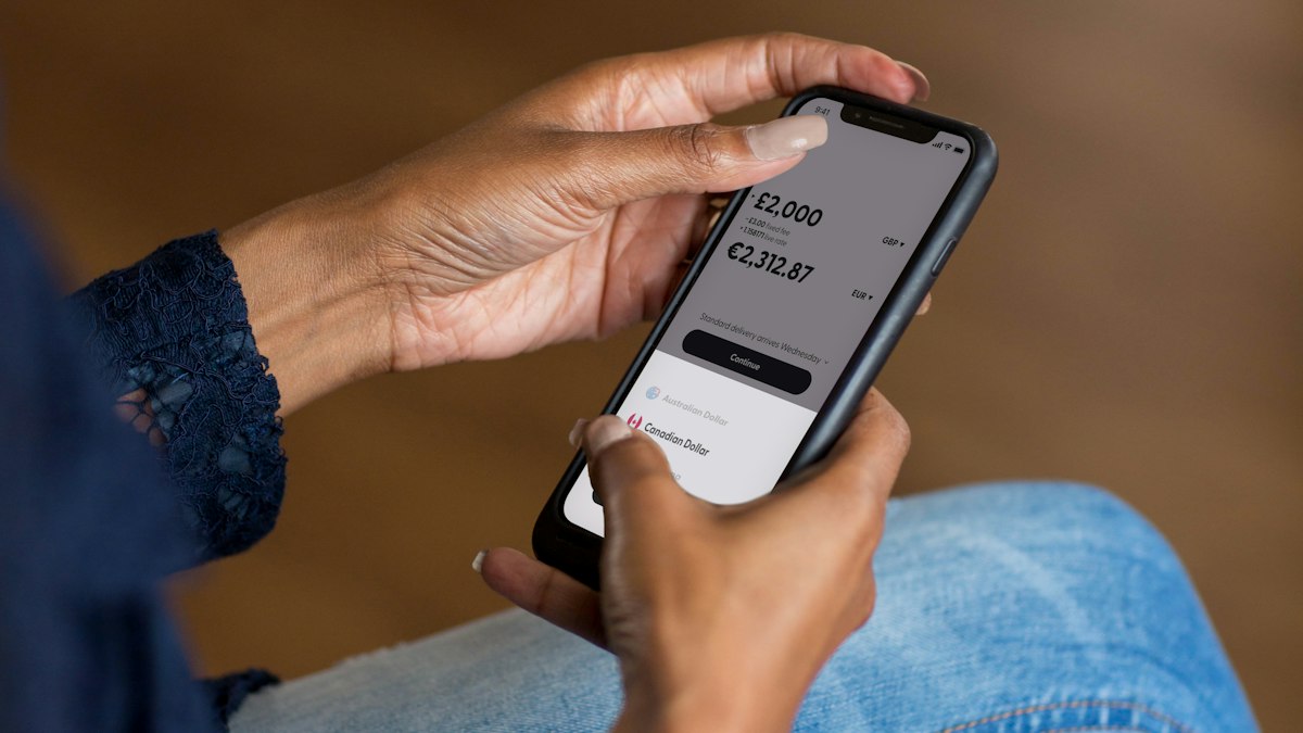 Mãos segurando um smartphone durante o uso de um aplicativo bancário para transferência de dinheiro