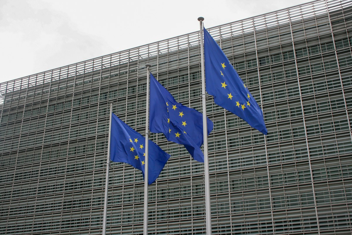 Três bandeiras da União Europeia hasteadas em frente a um edifício