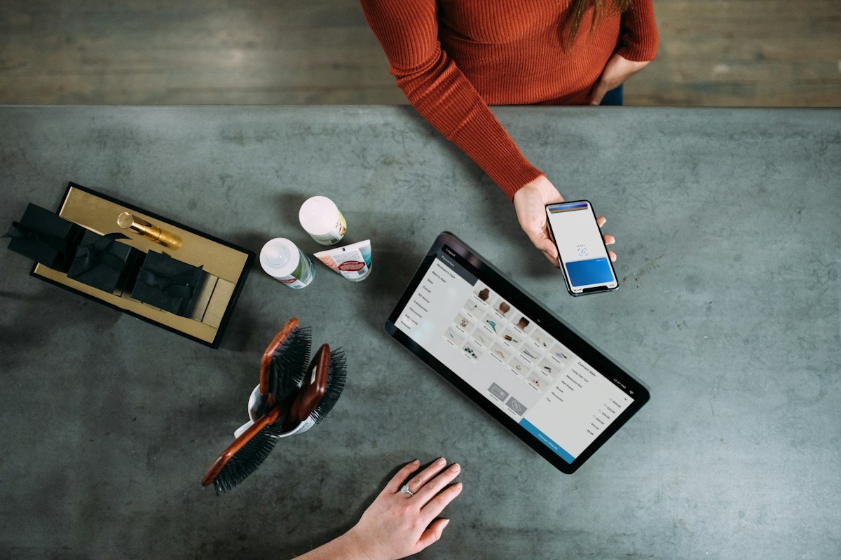 Pessoa segurando um smartphone ao lado de um tablet, cenário de compra online
